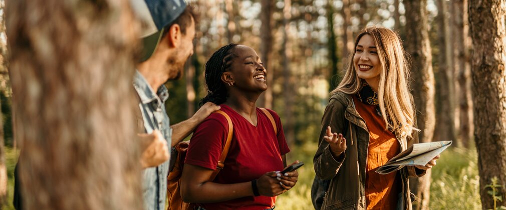 Three young people walk and talk through a forest landscape. 