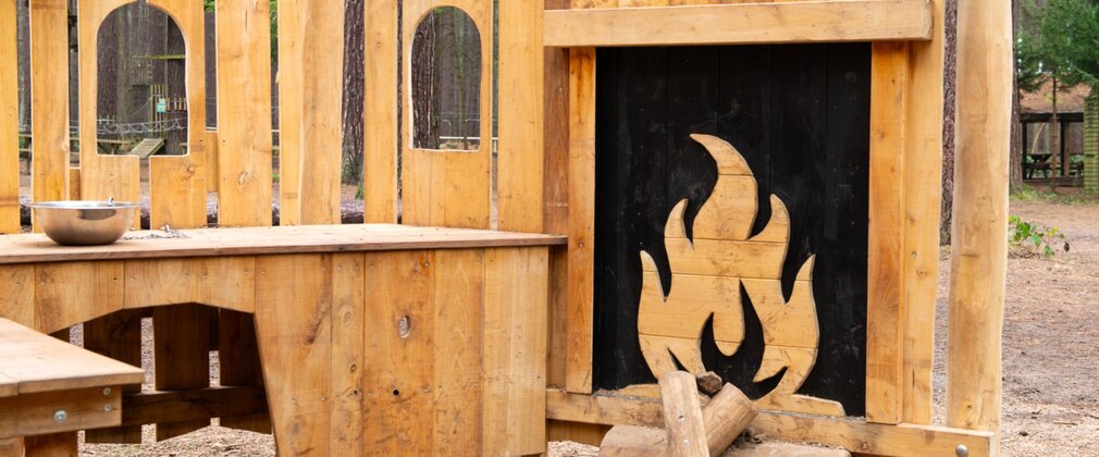A wooden play kitchen outdoors with pretend fireplace.