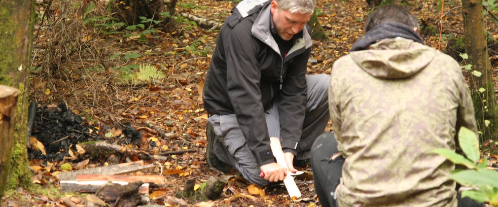 A man whittling wood with a knife in forest school 