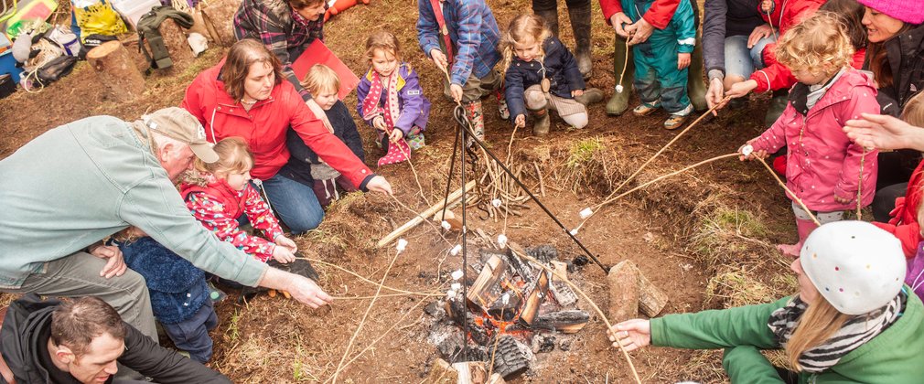 Large group of families sat around campfire toasting marshmallows
