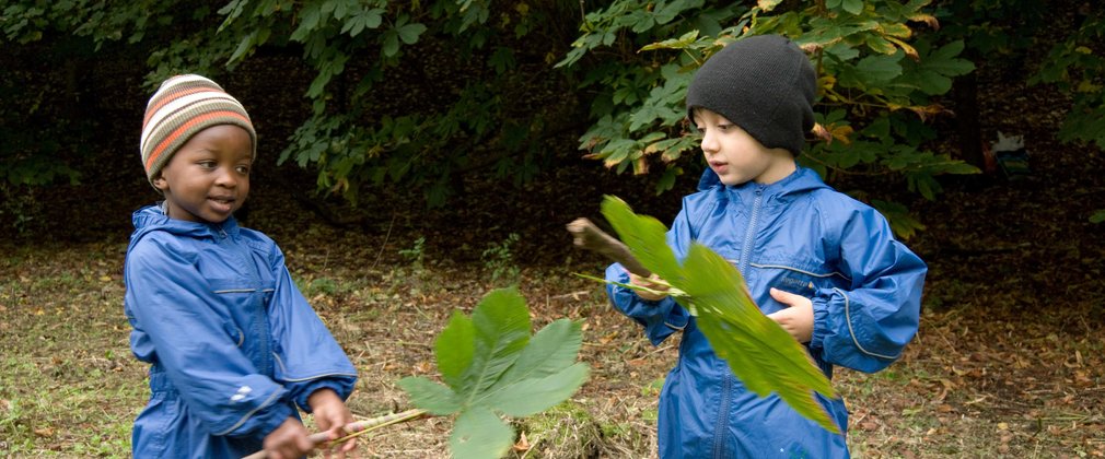 Two children playing with large leaves in the forest