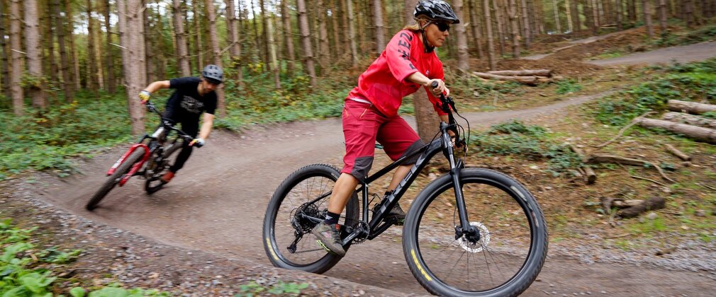 Two people ride mountain bikes along a trail through the forest.