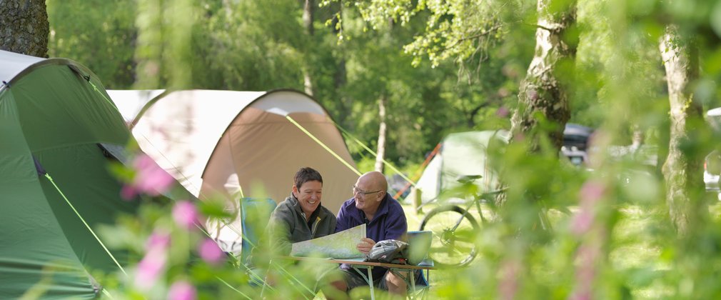 Couple sat next to tent within the forest 