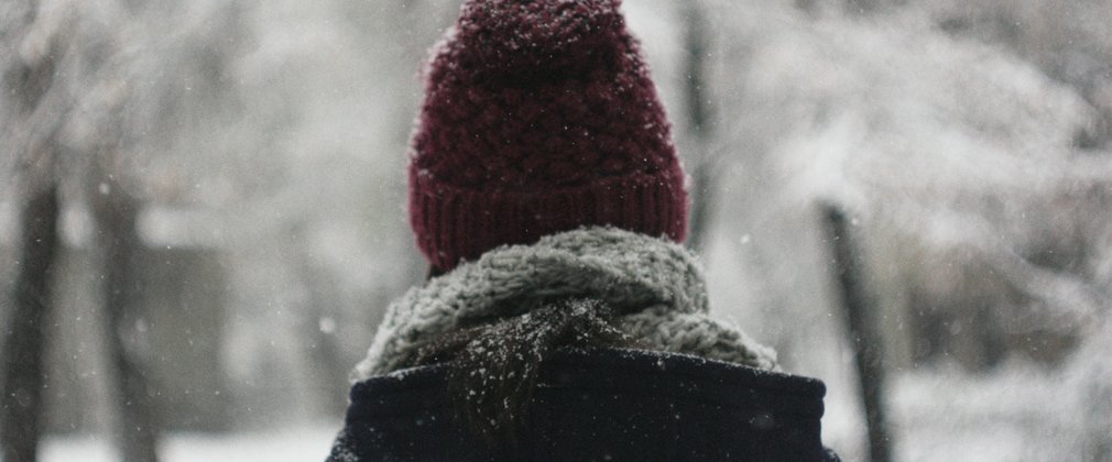 Woman in a red hat and blue coat looking at snow in the forest