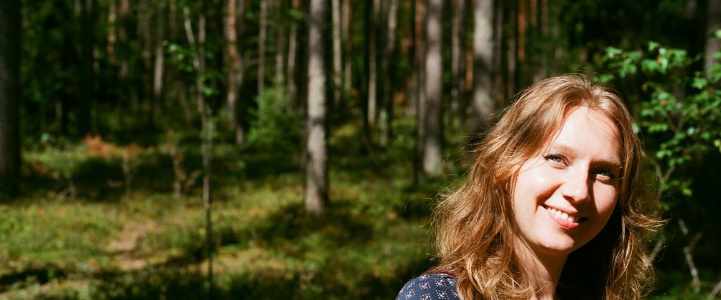 Fair haired woman smiles in the sunlight, with a forest backdrop