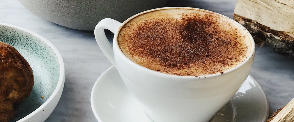 A cappuccino and croissant on a table with pieces of chopped logs