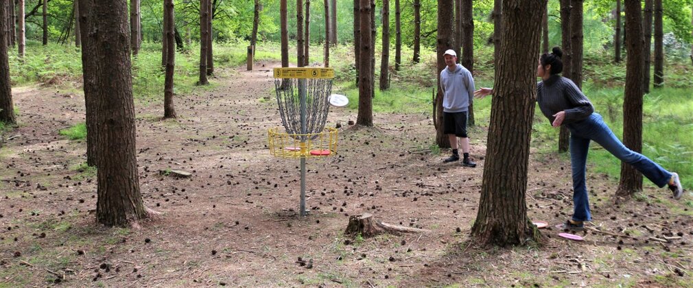 A man and woman playing disc golf among the trees.
