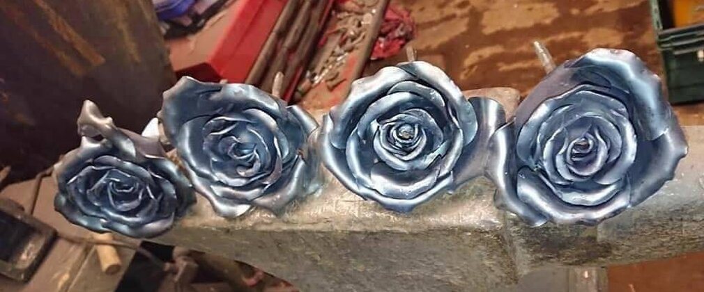 A row of metal forged roses laid on an anvil in a workshop