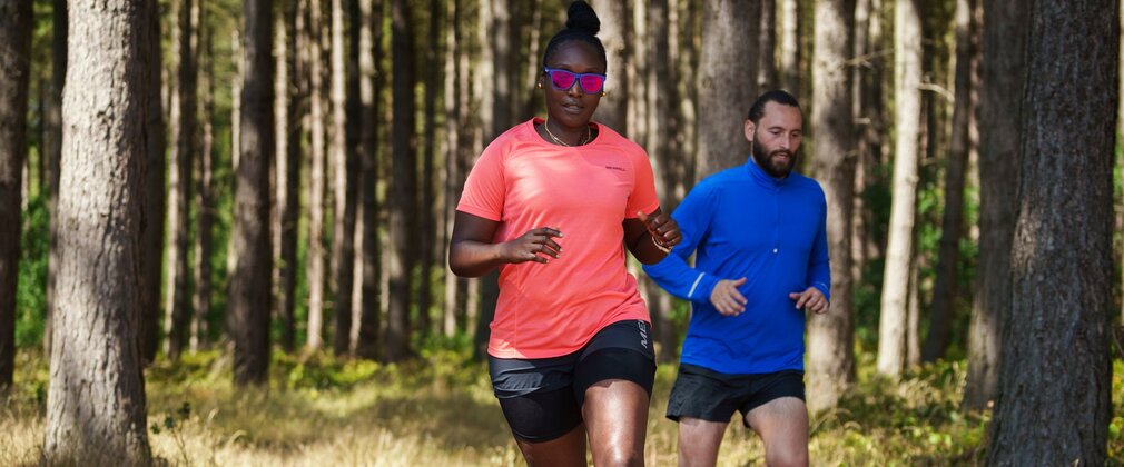 A man and a women in sports clothes, running in the forest.