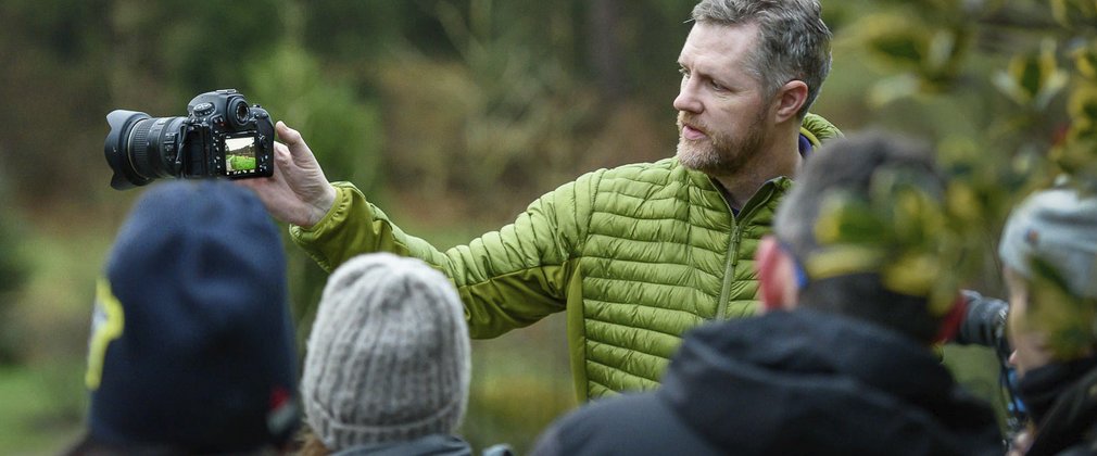 Man standing in a forest showing a group of people a camera