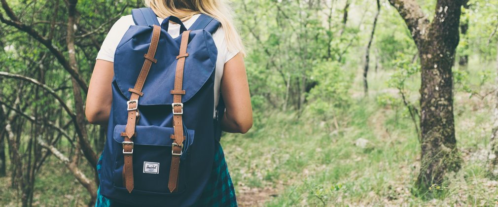 Women with blue backpack walking through spring woodland