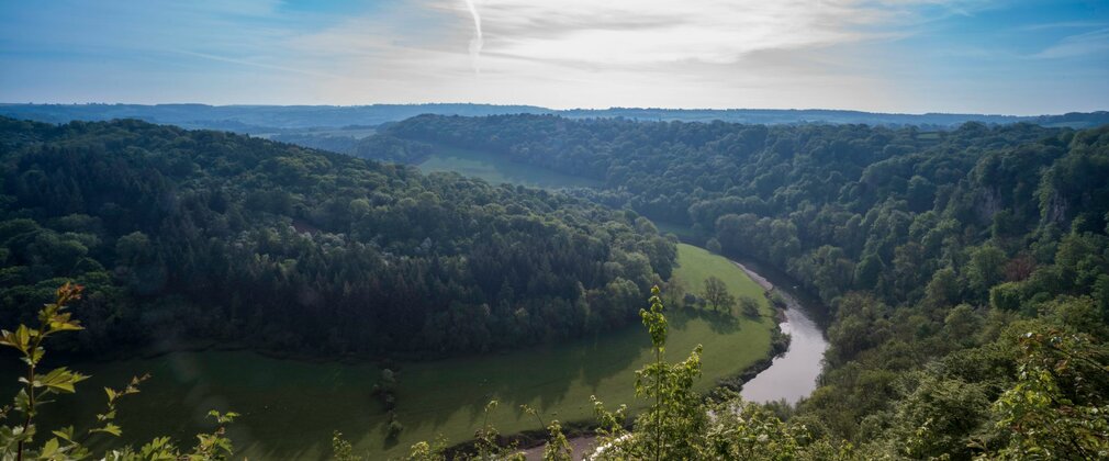 Looking down to a river winding through lush green landscape, against a blue sky.