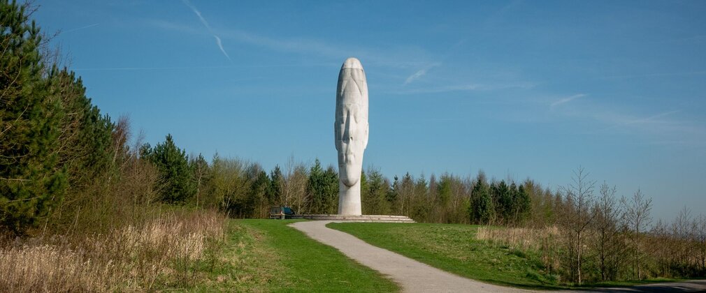 The Dream sculpture, a towering white head at Sutton Manor Country Park, viewed from a path through grassland.