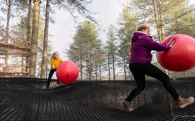 A child and an adult playing with exercise balls in the Go Ape Nets Adventure enclosure above the ground.