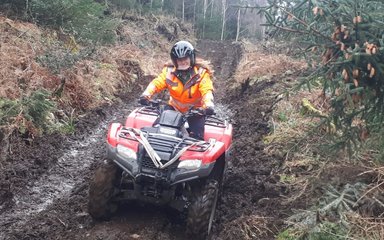 Woman forester driving a quad bike through a forest