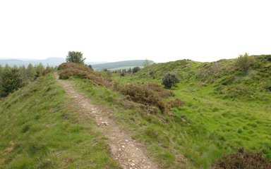 Small unsurfaced walking trail up a hill with rolling hills in the background