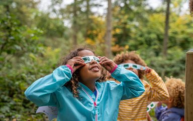 Two children with paper glasses looking up in a forest