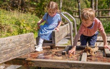 A girl and a boy playing with a piece of outdoor play equipment