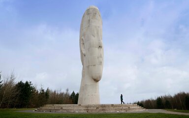 The Dream sculpture, a towering white head at Sutton Manor Country Park, viewed from a path through grassland.