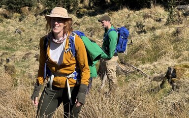 Woman in mustard jacket and cream hat walking uphill.