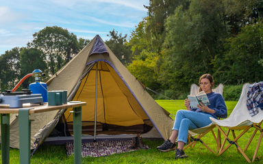 A woman reading sat next to a tent