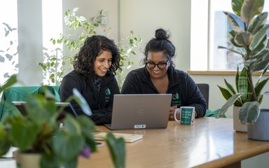 Two women smiling looking at a website in an office