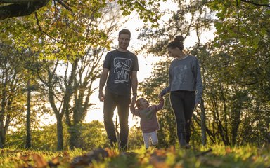 A family of three holding hands in the forest wearing Forestry England merchandise