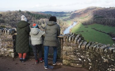 A family dressed in winter clothing looking out from Symonds Yat Rock viewpoint across the Wye Valley