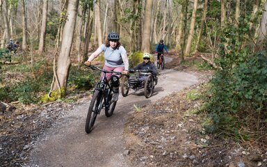 Three riders on different types of bike riding an accessible blue grade forest cycle trail