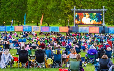 A large screen sits in front of a landscape of trees with Adventure cinema projected in the middle. Lots of people sit in deck chairs in front of the screen.