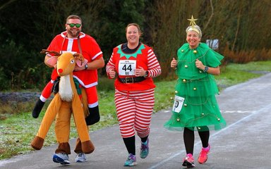 Three people running in a forest dressed as a reindeer, elf and Christmas tree