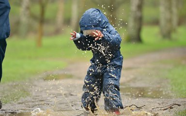 Child jumping in puddle and being splashed in the face 