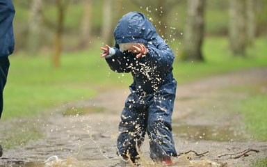 Child jumping in puddle and being splashed in the face 