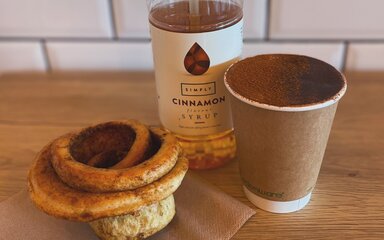 Cinnamon bun and takeaway coffee with a bottle of cinnamon flavoured syrup