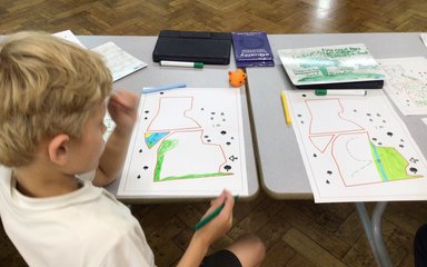 A young boy looks down at a piece of paper, he is colouring in a piece of land that he is designing for a replanting project at Westonbirt Arboretum