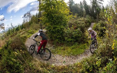 Two mountain bike riders through a turn on a singletrack forest trail