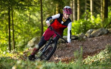 Mountain bike rider in red clothes leaning into a turn on a forest cycle trail