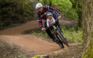 Man and child sharing a bike on a mountain bike trail