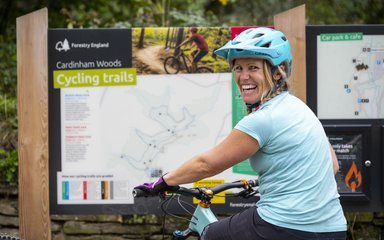 A female cyclist sitting on her bike and smiling over her shoulder with a map board in the background