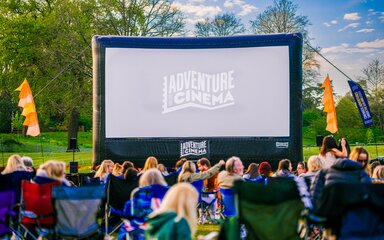 A large screen sits in front of a landscape of trees with Adventure cinema projected in the middle. 