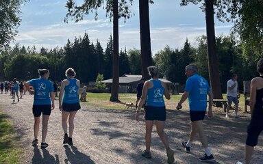 Four people wearing matching sports tops walking on a forest path with their backs to the camera.