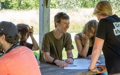 A young male smiles at a Westonbirt youth mentor who is talking through a task with the youth forum
