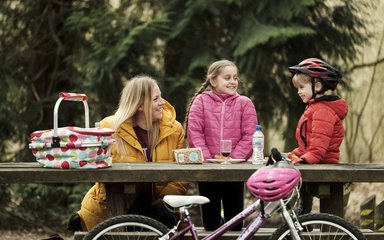 Woman and two children having a picnic on a picnic table in the forest