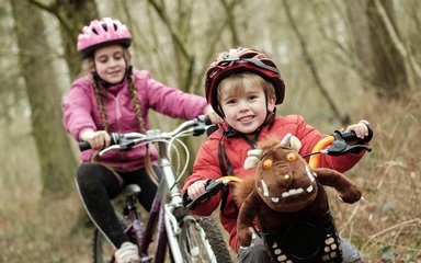 Two children on bikes, one with a Gruffalo toy in the front basket
