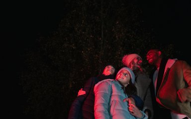 A family huddled together under red lighting looking up at the night sky