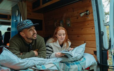 Couple reading a book in a campervan with the back door open