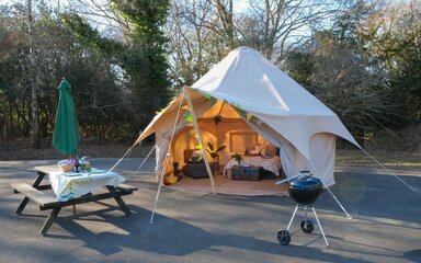 Bell tent furnished with cosy bedding with picnic bench and barbeque outside the tent
