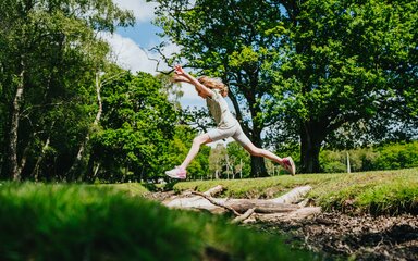 Girl jumping over a stream at New Forest campsite