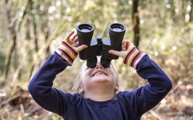 Child looking through binoculars in the forest