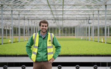 Man in uniform standing in glasshouse with seedlings behind